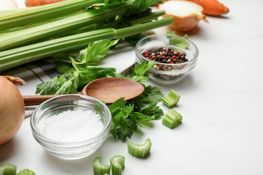 Fresh celery, spices, onion bulbs and wooden spoon on white table, closeup. Space for text
