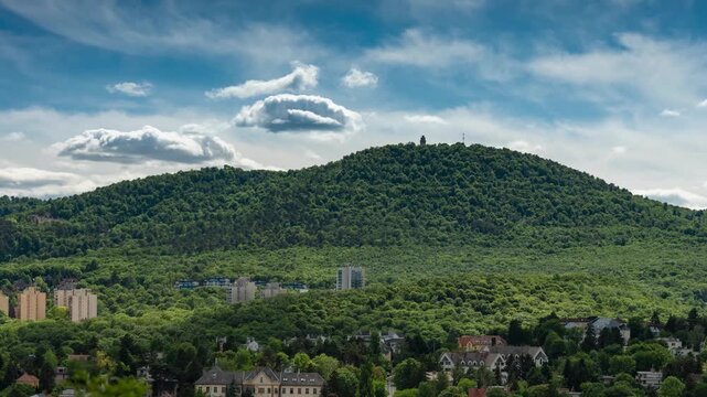 Budapest lush green Buda Hills timelapse with rushing clouds over Janos Hill and distant Elizabeth Lookout Tower at midday