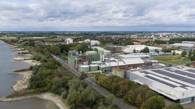 Monheim am Rhein, Germany - 04 September 2026: Aerial view of UNIFERM GmbH Co. KG industrial facility by the Rhine river, featuring storage tanks, factory buildings with solar panels, and greenery.