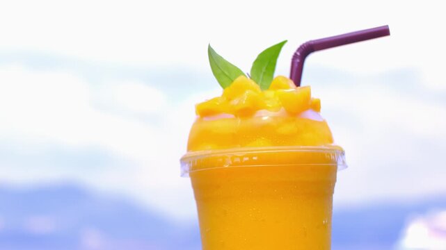 Smoothie made from fresh mango fruits against the backdrop of a seascape. Fruit and yoghurt ice cream decorated with leaves. Glass of tropical dessert close-up.