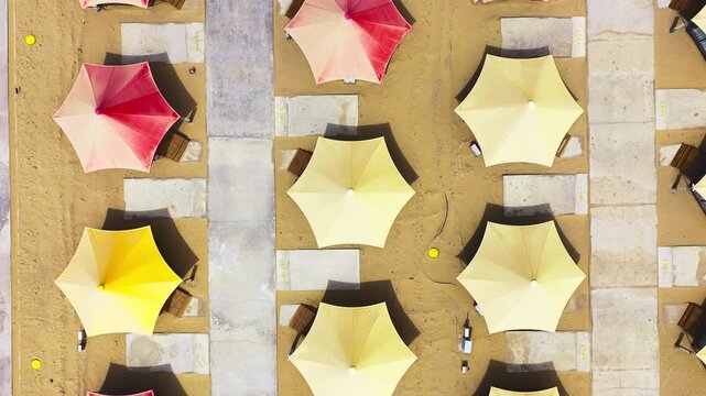 Top down aerial view of colorful parasols arranged in a desert camping site in Qinghai, featuring geometric sun shades on golden sand.