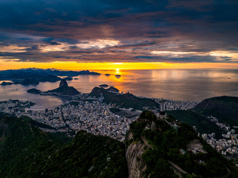 Rio de Janeiro, Brazil - 01 February 2025: Aerial view of Christ the Redeemer statue overlooking the city, Guanabara Bay, and Sugarloaf Mountain at sunset with golden light.