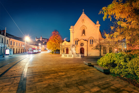 Illuminated night cityscape of Bratislava, capital of Slovakia, Europe. Exciting autumn view of empty street and Capuchin Church and Monastery. Traveling concept background.