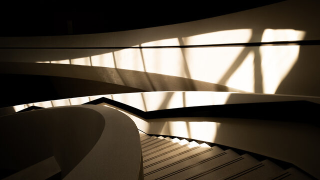 Abstract modern architecture with curved staircase walls and dramatic geometric sunlight shadows in minimalist interior
