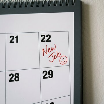 A close up view of a wall calendar showing a handwritten New Job reminder with a red ink smiley face icon on the twenty second day square for career change planning or professional growth