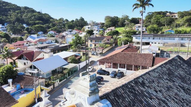 Aerial drone orbital shot focusing on the historic iron cross then pulling back to reveal the full colonial facade of Nossa Senhora das Necessidades church in Santo Antonio de Lisboa, Brazil.
