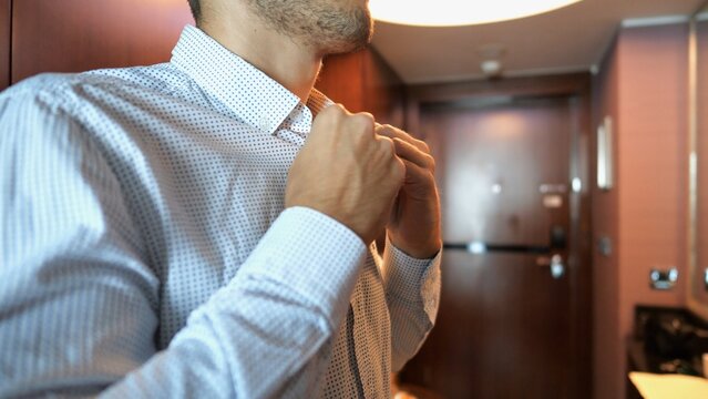 Close up of male hands of young businessman buttoning shirt cuffs in modern hotel room or apartment interior. Confident entrepreneur preparing formal clothing for business meeting or office work