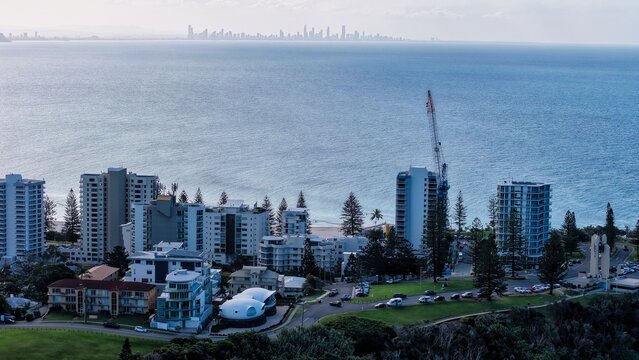 Tweed Heads, Australia - 15 August 2026: Aerial view of high-rise buildings along the coast with a construction crane, green parkland, and a distant city skyline visible across the ocean.