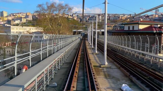 Rear view from a driverless metro train moving on an open elevated track and entering a tunnel in Istanbul. Urban rail infrastructure, cityscape and automated public transport on a sunny day