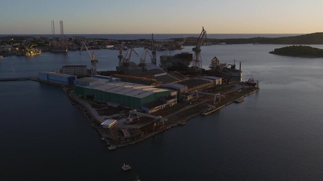 Aerial view of the Uljanik shipyard in Pula with industrial cranes, large warehouses, and ships docked in the harbor during the golden hour in Pula, Istria County, Croatia.