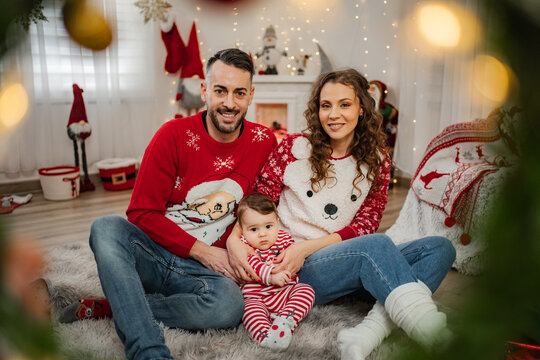 Family with baby celebrating Christmas holiday in festive sweaters at home