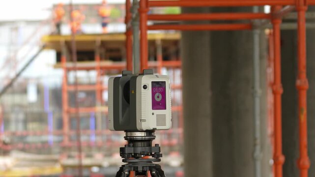 Moscow, August 30, 2026, Close-up of surveying equipment on tripod. Purple label with text visible. Orange scaffolding in background. Construction workers are working. Site activity captured clearly