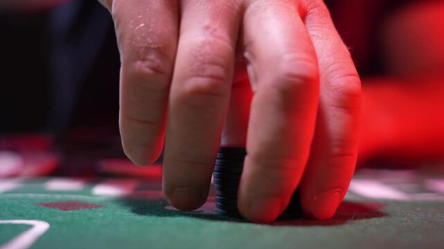 Green casino table surface close-up. Red sleeves conceal a clenched hand. Blue and red poker chips piled. White playing card center. Subtle tension implied. Ideal for gambling or casino content