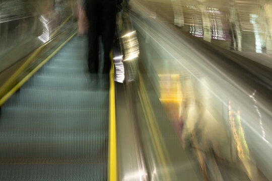 Intentional motion blur as moving up an escalator with bright yellow line and a person in black pants
