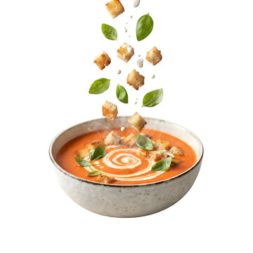 Tomato soup in a rustic bowl with falling croutons and fresh basil leaves isolated on transparent background