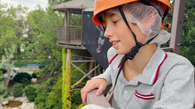  Kid in orange safety helmet on rope park zipline platform &mdash; side close-up