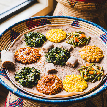 Traditional Ethiopian Beyaynetu Vegetarian Feast with Assorted Wats and Rolled Injera on a Handwoven Mesob Basket Tray