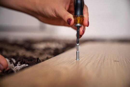Extreme close-up of a female hand tightening a screw into a wooden board using a manual screwdriver. DIY flat-pack furniture assembly, home renovation, repair work, and carpentry detail concept.