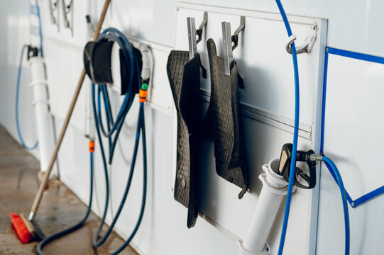 Car floor mats hang on clips at a self service wash bay where blue hoses are stored for cleaning