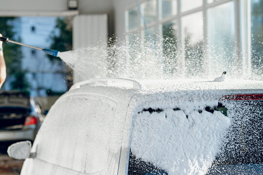 Person spraying water on a soapy vehicle to clean it at a professional service facility