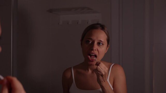 Young woman cleaning teeth with floss pick in mirror, performing oral hygiene routine and caring for gums at home