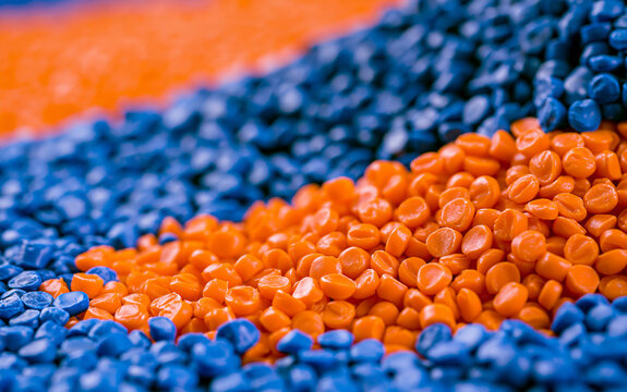 Close up of blue, orange plastic granules. Colorful polymer resin pellets pile up for industrial injection moulding process. Raw thermoplastic material beads used in manufacturing production