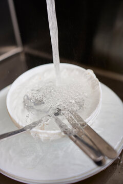 Water pours into stacked dishes and covers metal cutlery in kitchen sink