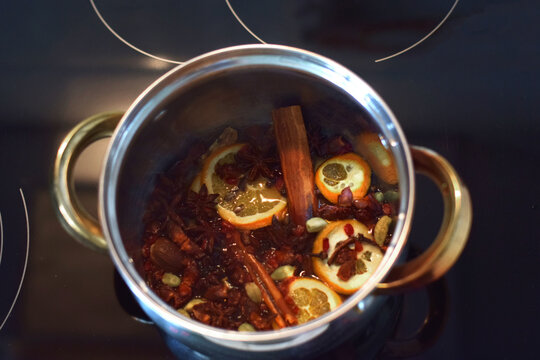 Sliced oranges, spices, and cinnamon simmer in a pot for mulled wine preparation. Ideal for culinary blogs, recipe sites, festive advertisements, and food magazine cooking features.