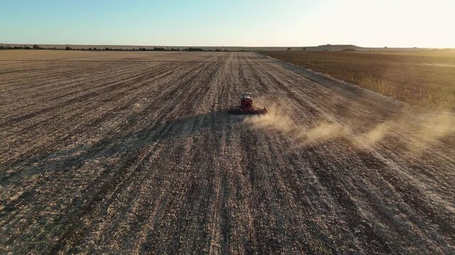 Aerial shot of a drone following a tractor plowing an agricultural field during golden hour sunset