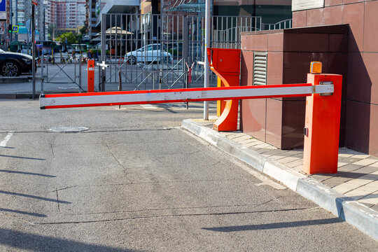 A red and white automatic barrier gate blocks a private parking entry lot on a city street. Urban security control access system layout. Transport theme.