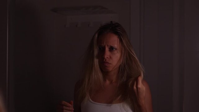 Young woman holding dry messy hair in the mirror, looking disappointed with frizz, dryness and damaged ends