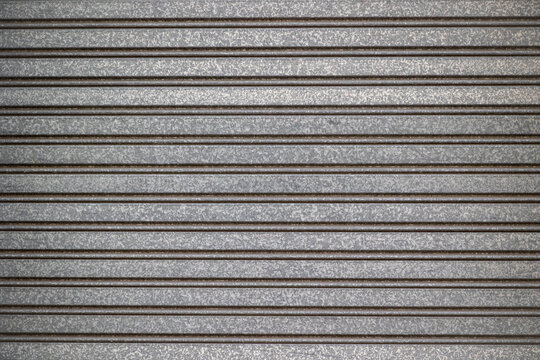Detailed gray galvanized metal panel featuring repetitive linear grooves, aged patina, soft highlights, and realistic metallic surface imperfections.