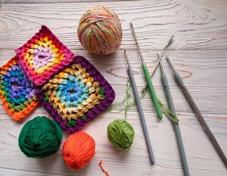 colorful woolen balls with multicolored granny squares and crochet hooks on white wooden ground