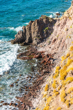 Rugged coastline on Lesbos, Greece, with turquoise Aegean waters breaking against volcanic rocks and steep cliffs covered in Mediterranean vegetation.