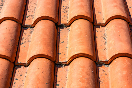 Close-up view of weathered terracotta roof tiles arranged in rows, highlighting their curved shapes, earthy tones and aged textures. Ideal for architecture, construction and heritage themes.