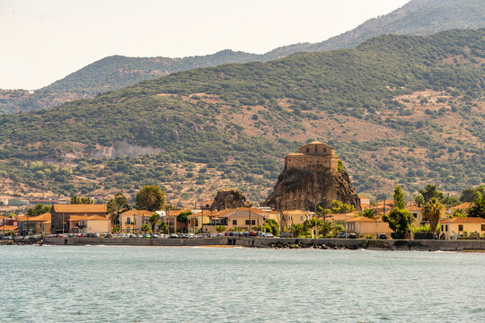 Panoramic view across Petra on Lesbos, Greece, of the Holy Church of the Virgin Mary Glykophilousa, a seaside village and rugged mountains glowing in warm evening light.