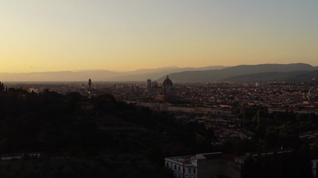Aerial view orbiting right over Florence at golden hour sunset, revealing historic center with Duomo Cathedral behind hills as commercial airplane takes off, Tuscany, Italy