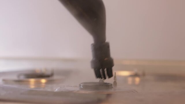 Handheld steam cleaner on stove top, powerful steam loosening burnt grease from stainless surface, closeup of nozzle and hand motion, countertop background, satisfying deep clean