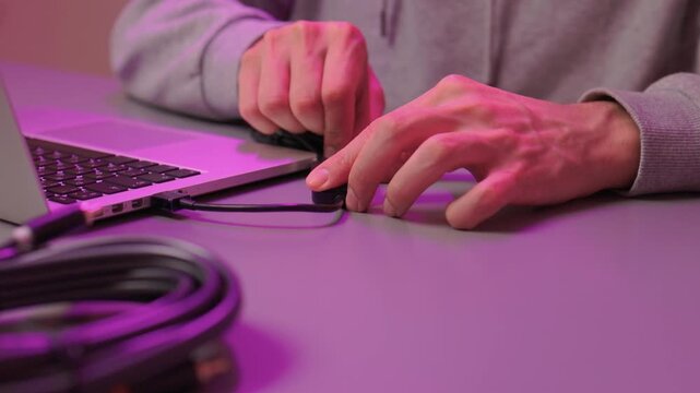 Preparing audio setup with focus on connection and ambient lighting. Attaching audio cable to laptop emphasizing precise finger placement and purple studio illumination