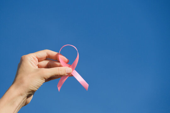 Pink breast cancer awareness ribbon held in woman hands against blue sky background in sunny day