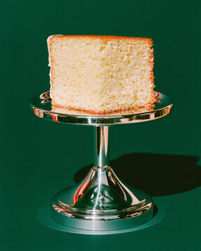 Plain sponge cake slice displayed on silver stand with green backdrop