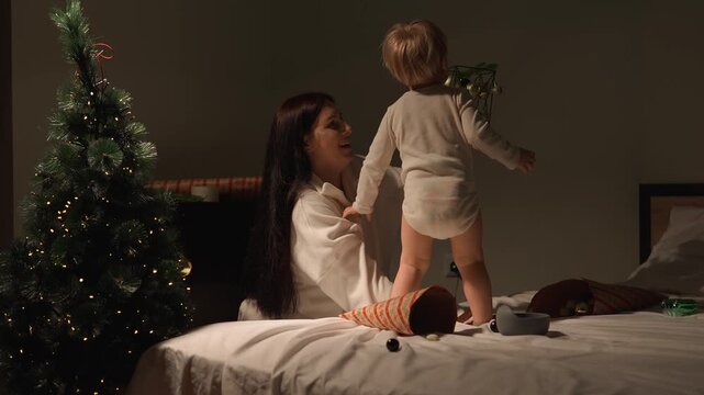 A toddler shares a festive home moment as he wears a paper party hat while his mother smiles beside him. The authentic moment presents New Year celebration, playful tradition and warm parenting.