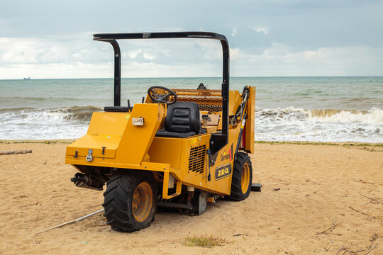 Varna. Bulgaria. 26.09.2026 yellow beach cleaning machine with roller and cage on sandy beach, cloudy sky and sea waves behind, industrial equipment outdoors, no people,  high qualit