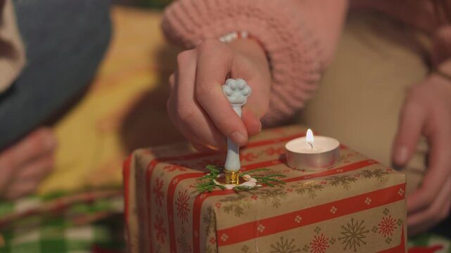 Detailed holiday footage captures hands as they pour melted sealing wax onto a carefully wrapped Christmas gift. Macro hand view presents traditional craft technique with strong commercial appeal.
