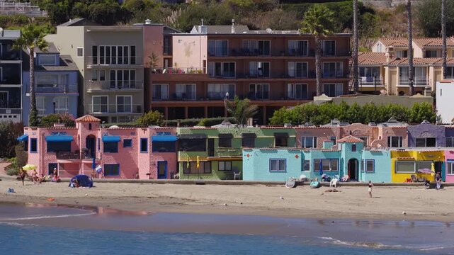 Aerial tracking pan shows the historic Venetian seaside village and sandy shoreline of Capitola Beach in California, with tourists relaxing by the ocean.