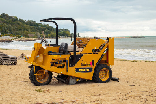 Varna. Bulgaria. 26.09.2026 yellow beach cleaning machine with roller and cage on sandy beach, cloudy sky and sea waves behind, industrial equipment outdoors, no people,  high qualit