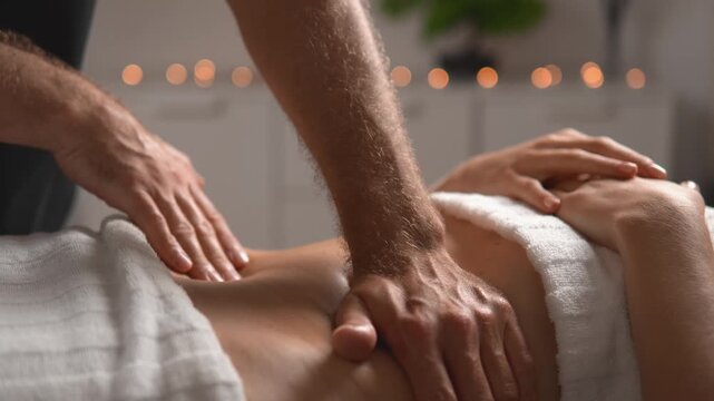 A massage therapist performs rhythmic manual massage over a woman's stomach and waist. The close angled view presents core relaxation, body care and client comfort for lifestyle media.