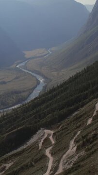 Aerial landscape of Katu-Yaryk Pass with steep dirt road switchbacks descending into the Chulyshman River valley, Altai Republic, Russia, in soft evening light