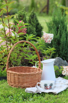 Wicker picnic basket with a light blue jug and fabric on a lush green lawn in a summer garden