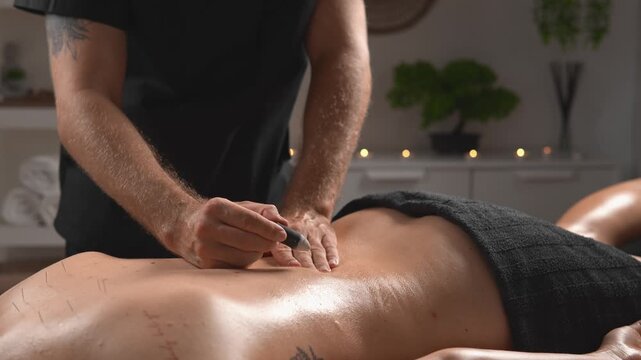 A massage therapist combines light manual pressure with acupuncture on the back. The medium overhead view presents integrative wellness, tension relief and client comfort.